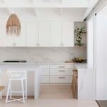 Hamptons kitchen with white Shaker doors, brass pulls, Calacatta-look stone waterfall island and rattan pendants