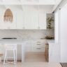 Hamptons kitchen with white Shaker doors, brass pulls, Calacatta-look stone waterfall island and rattan pendants