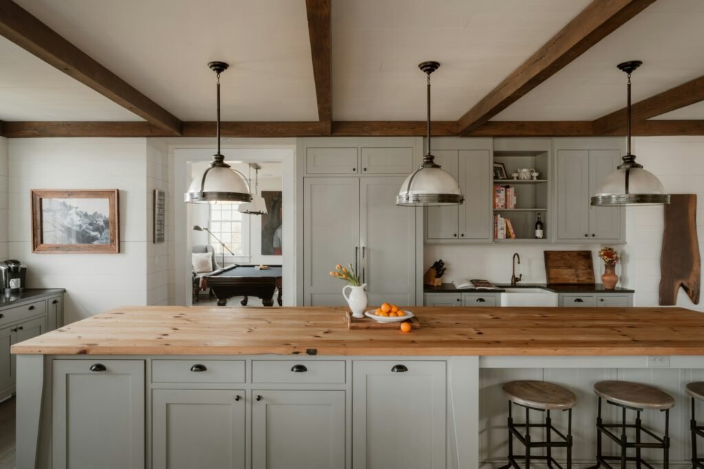 Modern farmhouse kitchen with grey-green Shaker cabinets, pine butcher-block island, farmhouse sink and exposed beams