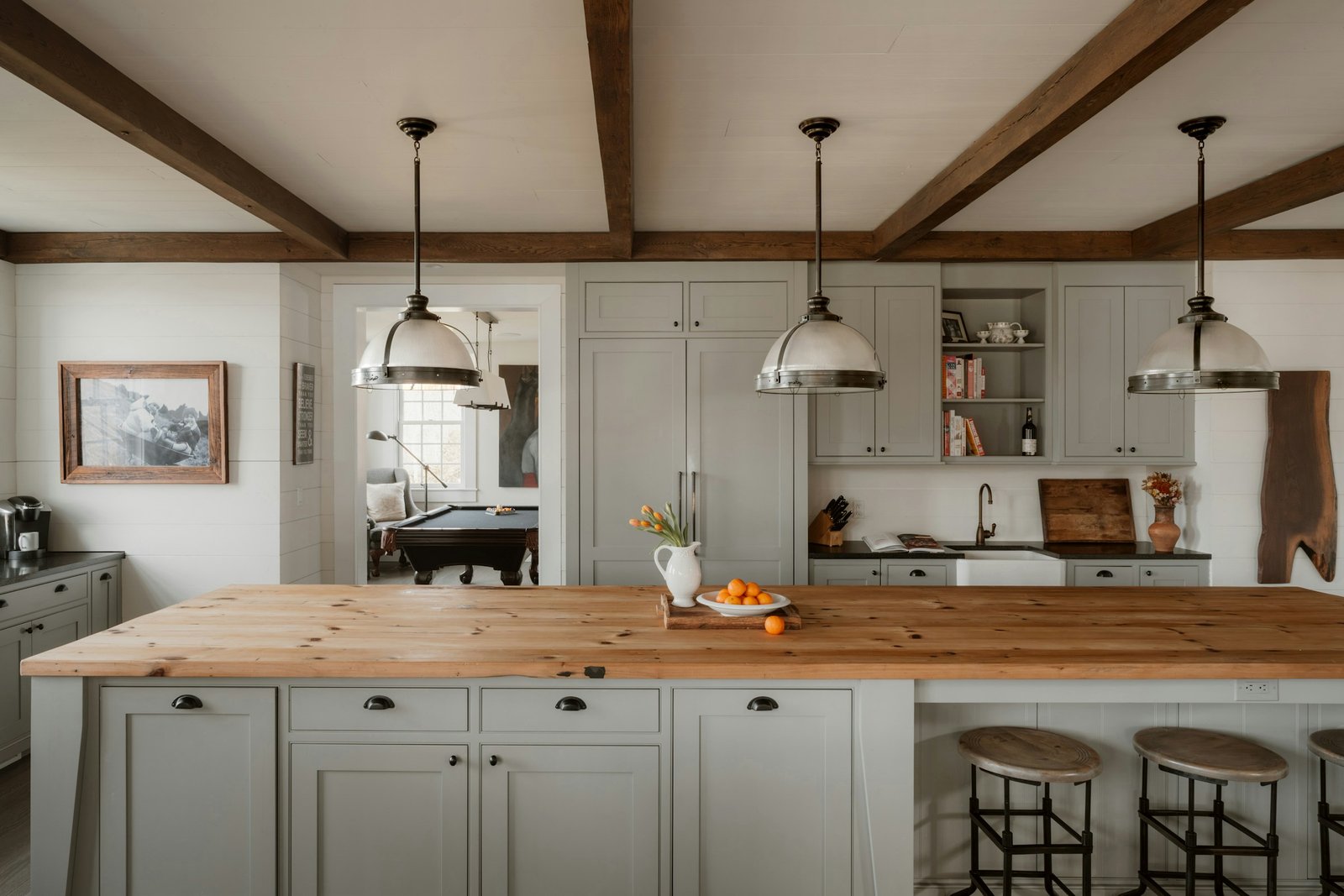 Modern farmhouse kitchen with grey-green Shaker cabinets, pine butcher-block island, farmhouse sink and exposed beams