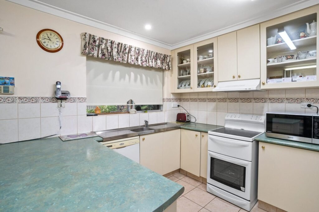 Before: the old kitchen next door, cream laminate cupboards, a green laminate benchtop and a freestanding stove