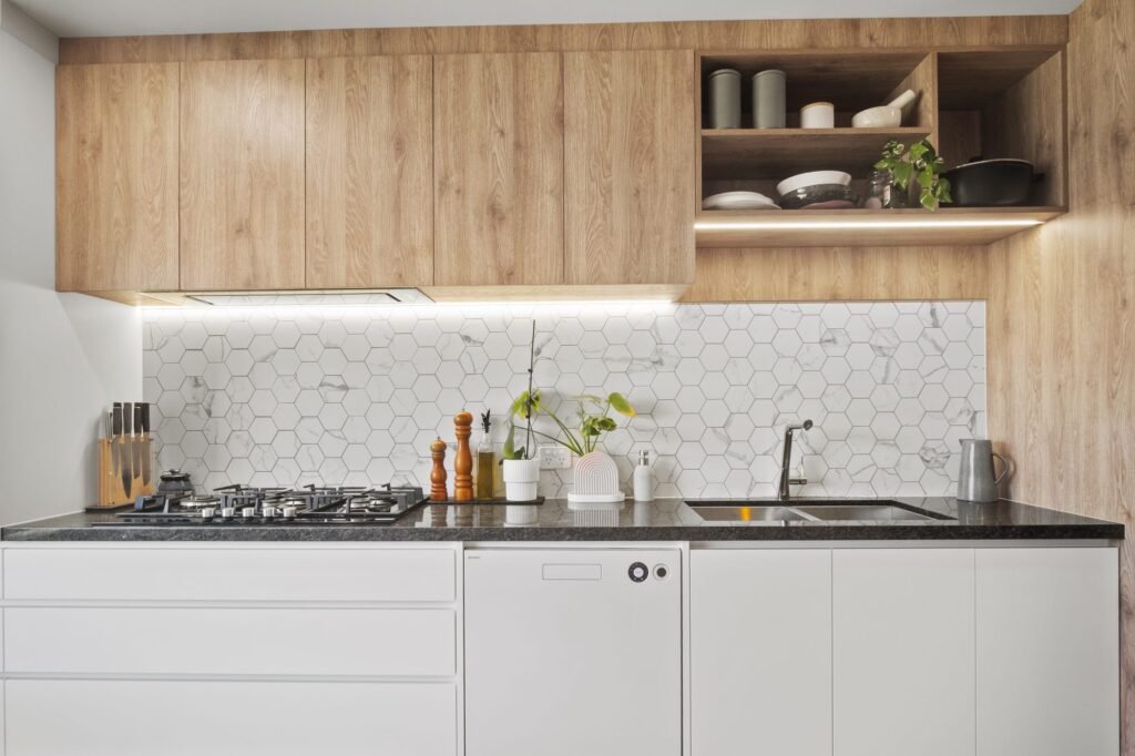 The cooking wall straight on: oak-look overheads with an open shelf, LED strip, hexagon tiles, five-burner gas cooktop, white handle-free drawers
