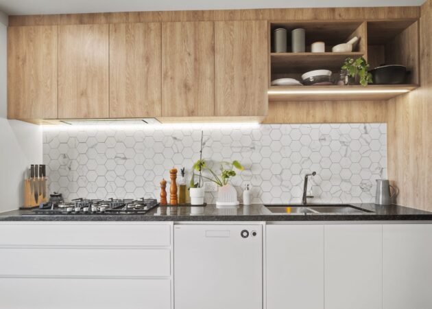 The cooking wall straight on: oak-look overheads with an open shelf, LED strip, hexagon tiles, five-burner gas cooktop, white handle-free drawers