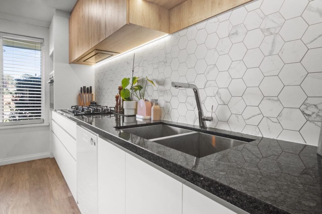 The sink run: double undermount sink, gooseneck mixer, dark speckled stone, slim rangehood under the overheads