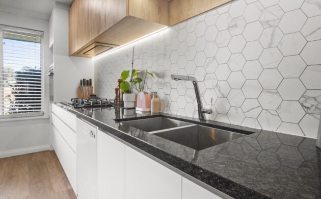 The sink run: double undermount sink, gooseneck mixer, dark speckled stone, slim rangehood under the overheads