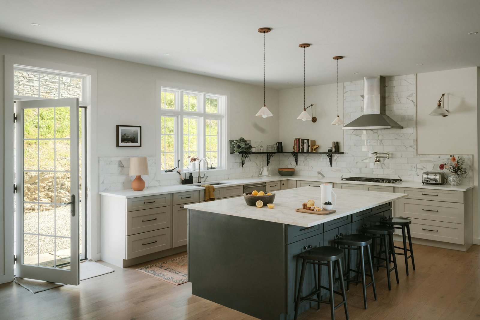 Deep green kitchen island with a marble top and black stools in a white kitchen