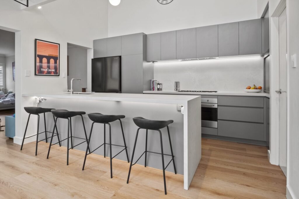The peninsula in honed Cloudburst Concrete with its waterfall end, four black stools, grey handle-free cabinetry behind