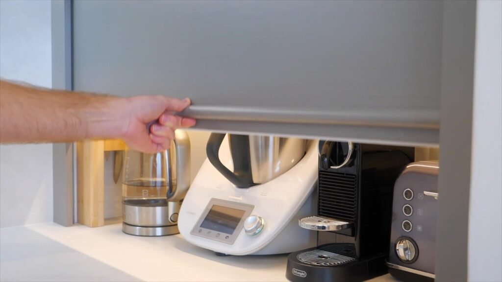 The roller door rising on the corner cabinet that wraps the waste pipe, the appliance station behind it