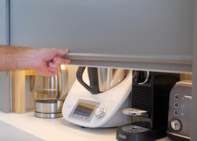 The roller door rising on the corner cabinet that wraps the waste pipe, the appliance station behind it