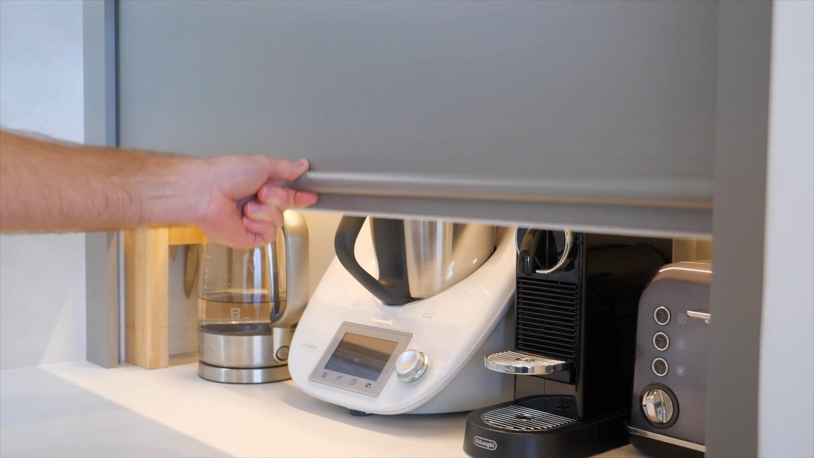 The roller door rising on the corner cabinet that wraps the waste pipe, the appliance station behind it