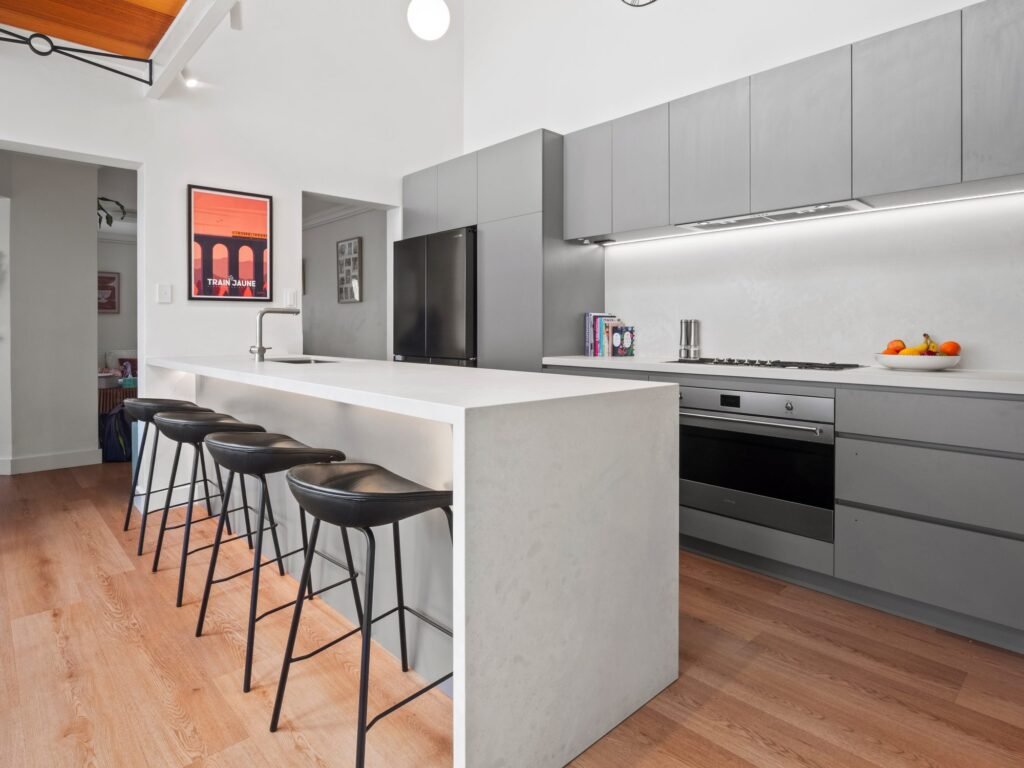 The whole kitchen: grey cabinetry, the peninsula, the mezzanine walkway above