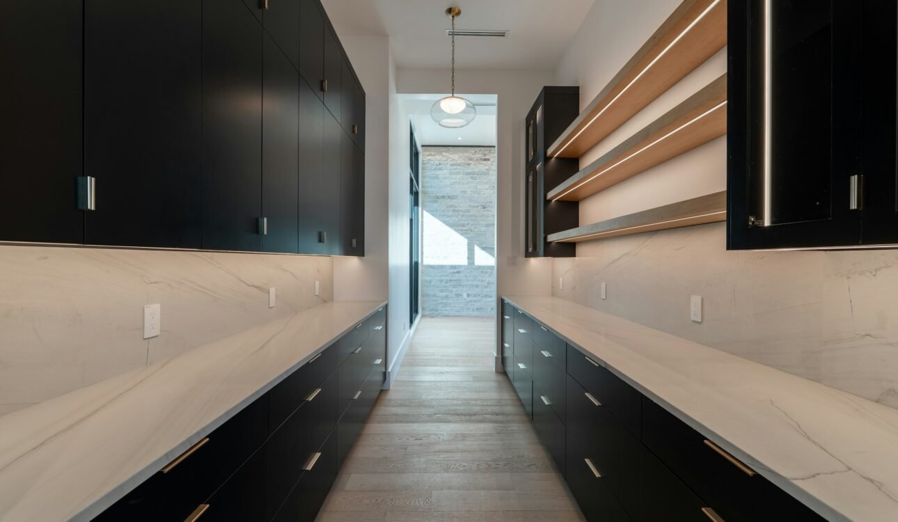Scullery with black cabinetry, marble benchtops and oak open shelves running the length of a galley