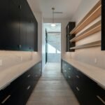Scullery with black cabinetry, marble benchtops and oak open shelves running the length of a galley