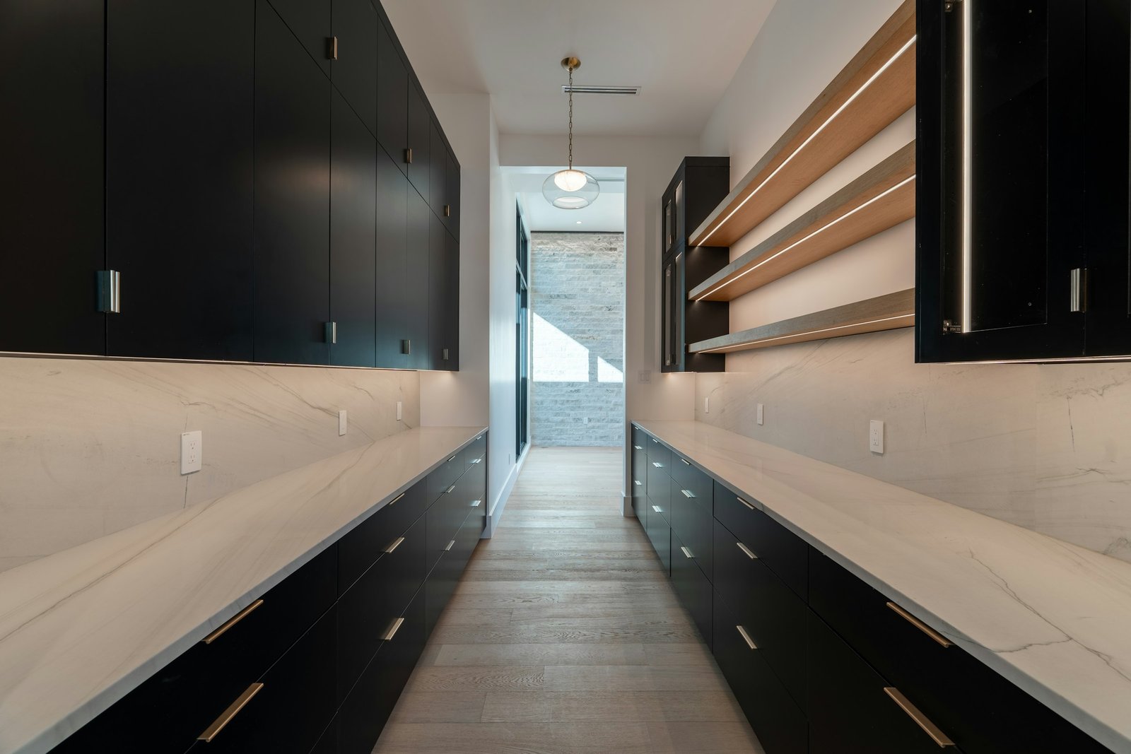 Scullery with black cabinetry, marble benchtops and oak open shelves running the length of a galley