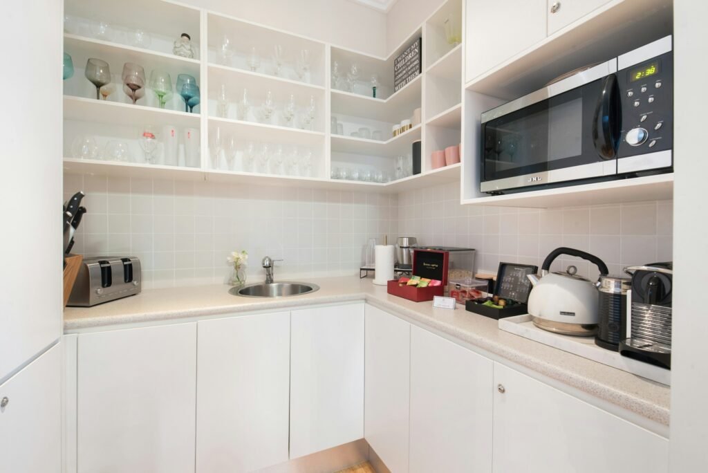 White scullery with a sink, microwave shelf and open shelving for glassware