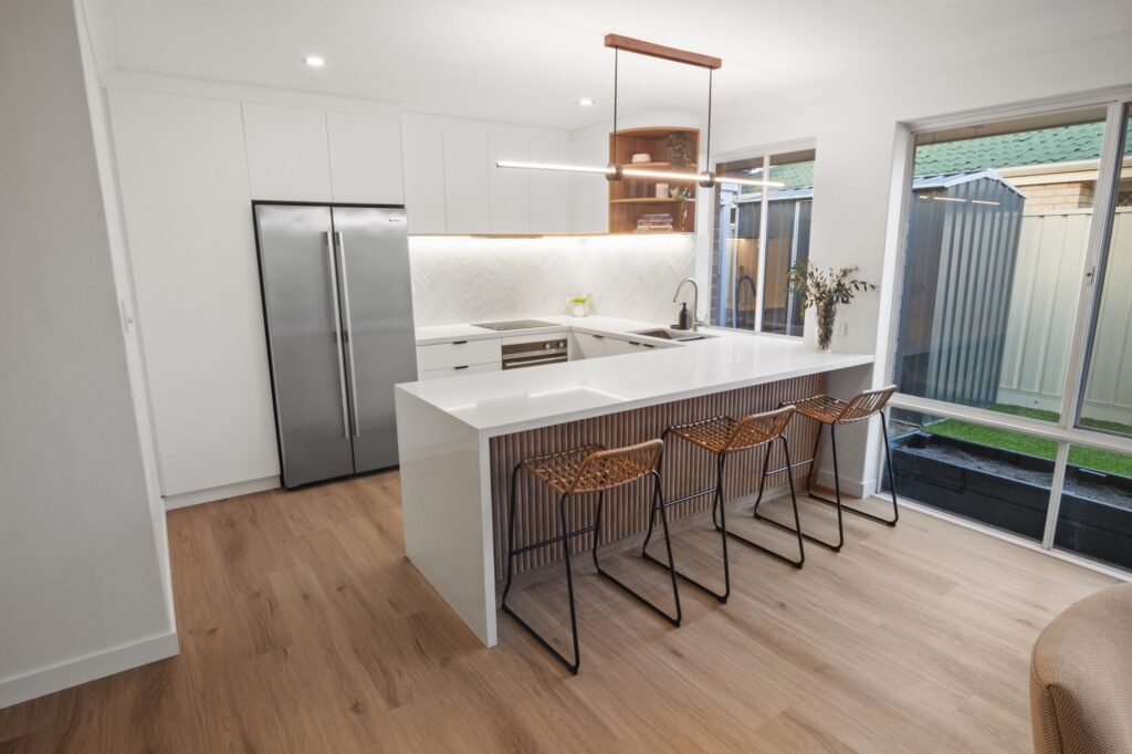 The batten peninsula with three cane stools, the stainless fridge and the white herringbone splashback