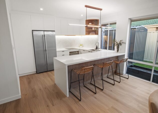 The batten peninsula with three cane stools, the stainless fridge and the white herringbone splashback