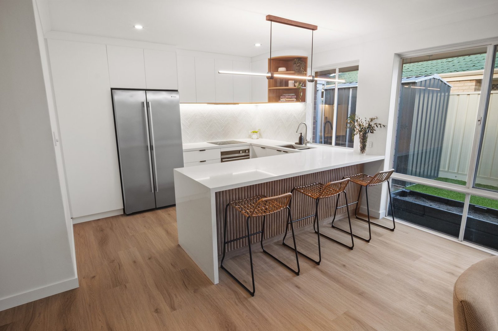 The batten peninsula with three cane stools, the stainless fridge and the white herringbone splashback