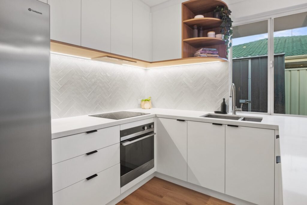 The corner: induction cooktop, under-bench oven, sink, herringbone tiles and the rounded Boston Oak shelves
